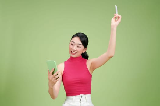 Young Asian businesswoman sitting on box and showing credit card and mobile phone isolated on green