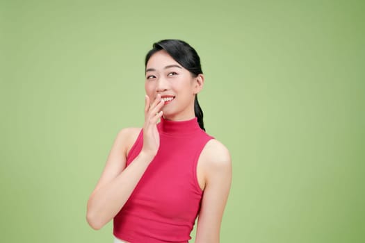 Asian young shying embarrassing female model smiling hold hand cover mouth laughing on green