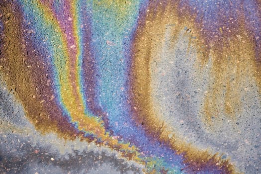 Close-up of an iridescent oil or gasoline spill on a wet asphalt, viewed from above. Bold multicolored spots on the asphalt. Concept of environmental problems