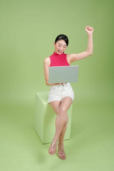 Beautiful Asian woman sitting podium, working with laptop isolated on green background.