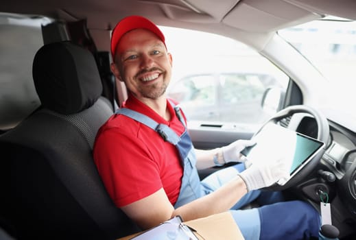 Man courier sitting behind wheel of car and holding digital tablet in his hands. Freight logistics concept