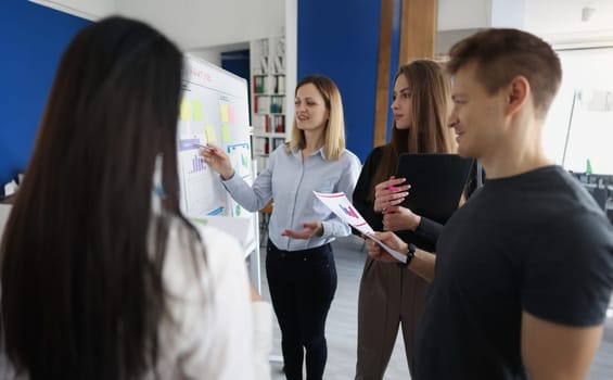 Young woman trainer showing information on board with graphs for listeners. Business education concept