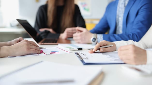 Group of business people are sitting at table with laptop and documents with charts closeup. New modern approaches to development of small and medium-sized businesses concept