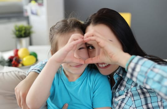 Little girl and mother hugging and showing heart together with their hands. Child care concept