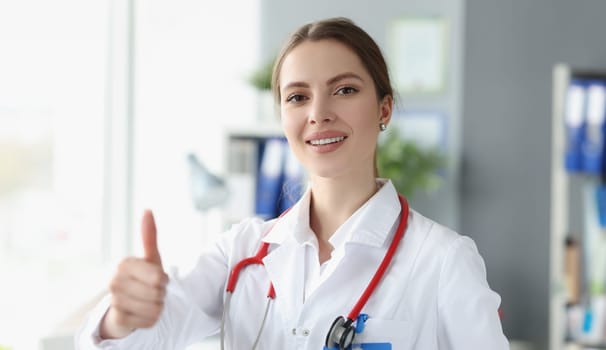 Smiling woman doctor showing thumb up in clinic. Quality health insurance concept