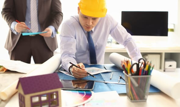 Male Architector Working on Construction Project. Freelance Group do Building Design. Architect or Engineer in Hardhat Writing on Blueprint, Architectural Concept. Engineering Tools Elements at Table