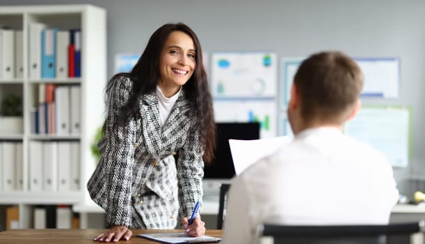 Portrait of pretty smart businesswoman posing on camera and signing contract. Smiling female in presentable costume in company office. Finance and economy concept