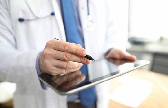 Close-up of professional doctor holding modern tablet and pen. Detailed picture with medical worker in office. Qualified specialist wearing uniform. Medicine and checkup concept