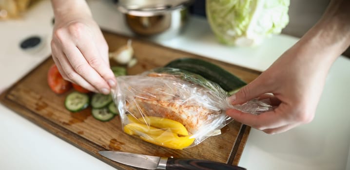 Close-up of womans hand cooking delicious meal for family. Adult prepare vegetables for baking in oven. Yummy and healthy food. Cooking on wooden cutting board. Sharp knife. Cuisine concept