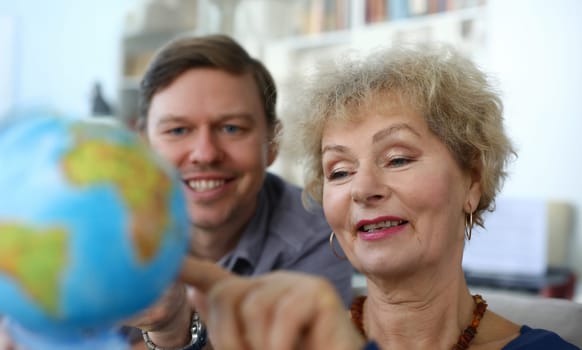 Close-up of senior good-looking woman and middle-aged man explore globe. Mother and son decide where to travel next. Modern technology and spare time together concept