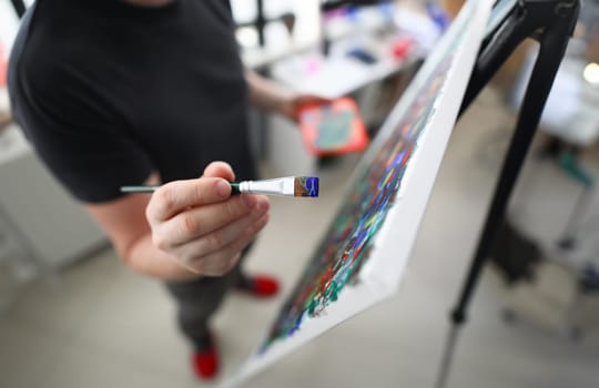 Top view of person creating new masterpiece with paintbrush. Mans hand holding brush and applying blue colour on canvas. Fresh idea for painting. Hobby for soul and leisure concept