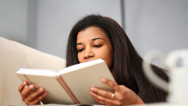Smiling black woman read story book at home preparing for college exams