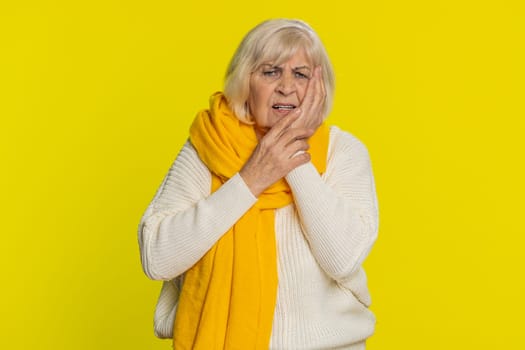 Dental problems. Senior old woman touching cheek, closing eyes with expression of terrible suffer from painful toothache, sensitive teeth, cavities. Mature grandmother pensioner on yellow background