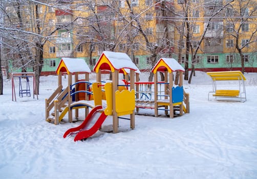 Children's play ground in snow with residential building on the background. Winter season in Krasnoyarsk city