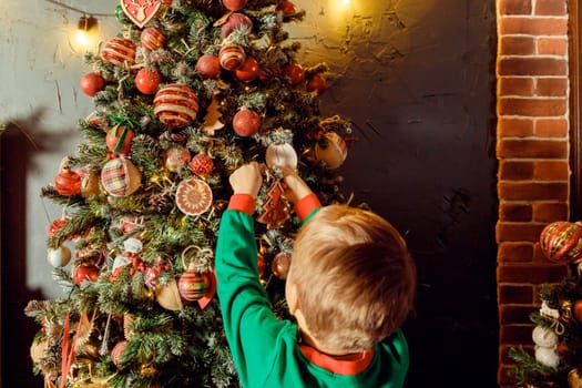 Child hanging a Christmas boot decoration illuminated on a Christmas tree from colorful ambient glowing lights.