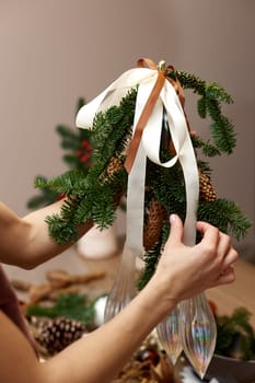 Woman making Christmas arrangement with fir branches, pine cones and bow. craft handmade decor.
