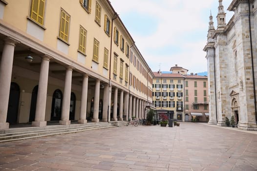 Como, Lombardy, Italy. Photography of empty street in in the center of Italian city of Como, with columns near the entrance of medieval cathedral of Santa Maria Maggiore. Beautiful architecture