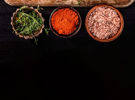 helps spices and salt in bowls on a black table, top view with copy space