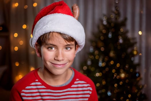 Smiling boy in Santa red hat on Christmas tree background and lights. Christmas concept