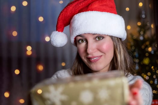 Smiling Woman in Santa hat with new year gift in background of lights