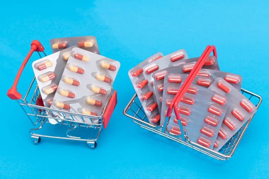 Buying Medicines. Drug Addiction Concept: Pills and Capsules in Shopping Cart on Blue Background. Global Pharmaceutical Industry and Big Pharma. Ordering Pharmaceutical Products