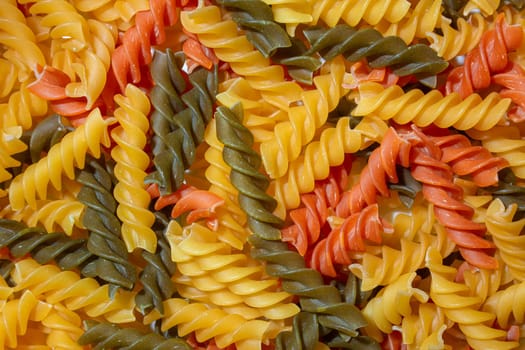 Uncooked Vibrant Colored Fusilli Pasta: A Mesmerizing Culinary Canvas of Multicolored Spirals, Creating a Lively and Textured Background for Gourmet Cooking. Colored Dry Pasta. Raw Macaroni