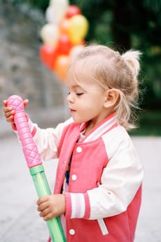 Little girl examines a toy sword in a scabbard in her hands while standing in the garden. High quality photo