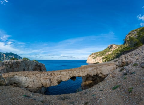 Impressive rock arch on Ibiza's coast, contrasting with blue sky and turquoise sea.