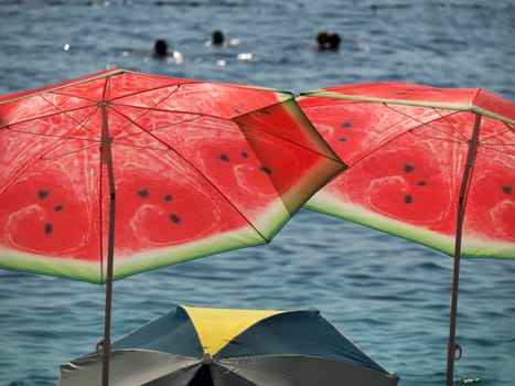 Watermelon sun umbrella on the beach ofcrystal clear water of Adriatic sea in Brela on Makarska Riviera, Dalmatia Croatia