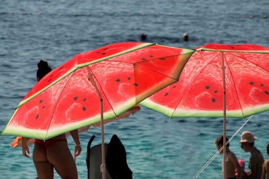 Watermelon sun umbrella on the beach ofcrystal clear water of Adriatic sea in Brela on Makarska Riviera, Dalmatia Croatia