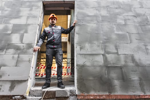 A construction worker in overalls stands in the opening of a building under construction, copy space.
