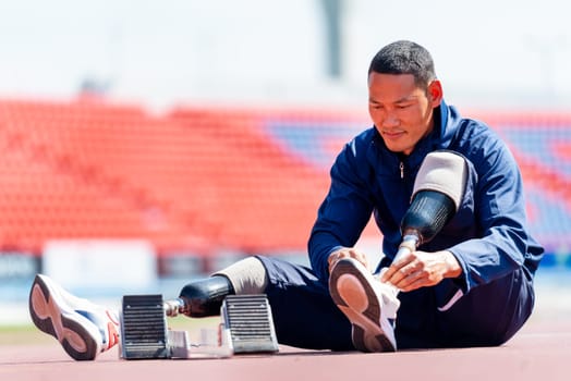 Sport man athlete with a prosthesis on his leg sit near the running equipment to tie shoelaces on the track at the stadium. Sport concept.