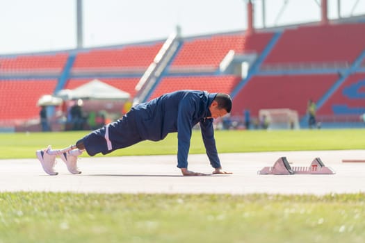 Sport man athlete with a prosthesis on his leg action of warm-up the body before exercise by do the push-ups near the running equipment on the track at the stadium, sport concept.