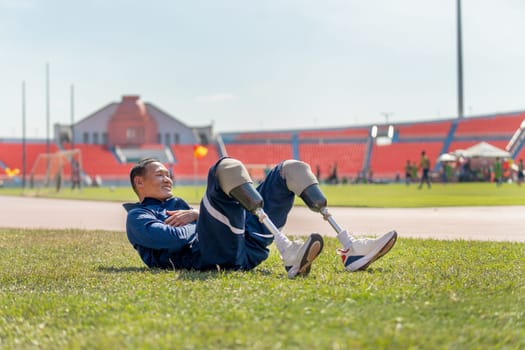 Sport man athlete with a prosthesis on his leg action of warm-up the body by lie down on grass field and bend body up to stretch his abdomen at the stadium, sport concept.