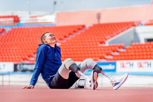 Sport man athlete prosthesis legs sit on the track and look over at the stadium to relax after exercise with happiness.
