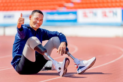Sport man athlete with a prosthesis on his leg sit on the track and show thumbs up after exercise at the stadium. Sport concept.