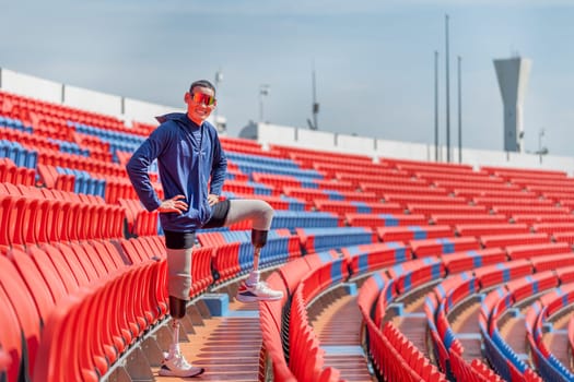Sport man athlete prosthesis legs stand with put one leg on chair of amphitheater also look at camera in the stadium with smiling.