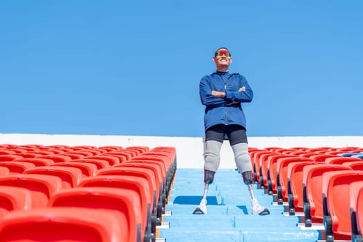 Sport man athlete prosthesis legs stand with arm crossed on stairs with happiness on amphitheater in the stadium with day light.