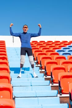 Vertical image of sport man athlete prosthesis legs stand on stairs with action of happy and celebration on amphitheater in the stadium with day light.