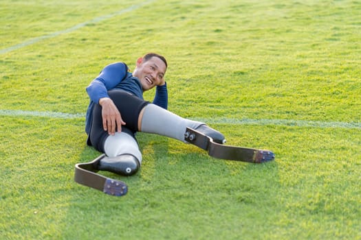 Sport man athlete prosthesis legs lie down on grass field to relax also look at camera with smiling in the stadium.