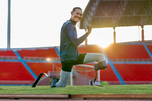 Close up sport man athlete prosthesis legs stay in the position of stretching and push his muscles also look at camera in the stadium with soft light of evening.