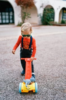Little girl in sunglasses looks at a toy cart while standing on the road. High quality photo