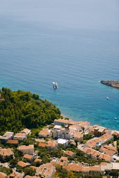 Motor yacht floats on the sea from the shore of an old town with red roofs. Top view. High quality photo