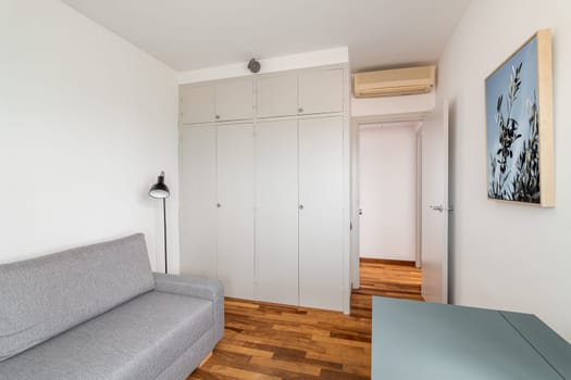 Large wardrobe, grey sofa and desk in empty room. Home interior with stylish furnishing for comfortable life. Cosy flat rental service