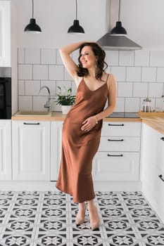 Smiling attractive young woman wearing silk long dress dancing at the kitchen at home