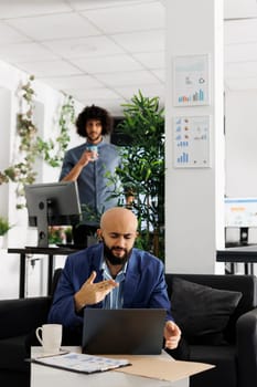 Arab entrepreneur presenting business plan to team during video conference call using laptop. Executive manager discussing product launch in videocall while sitting on couch in coworking space