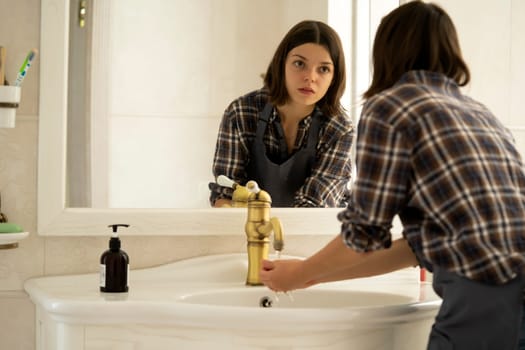 The girl creates cleanliness in the bathroom, cleans her spacious comfortable house using detergents, the woman washes her hands with soap near the mirror.