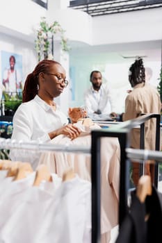 Clothing shop assistant adjusting display rack to showcase jackets new collection for customers. African american woman arranging fashion apparel merchandise in department store