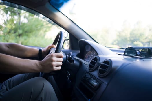 A young man travels in his car, drives along the road at sunset, holds the steering wheel with his hands, closeup view.