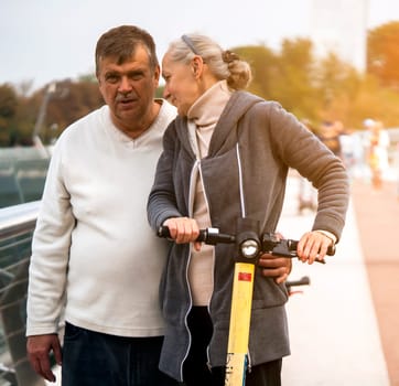 Elderly happy couple have a good and fun time together, on a walk riding a scooter in the park, an elderly man and his wife lead an active and healthy lifestyle.